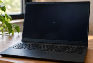 Black Lenovo laptop on a wooden desk with a small bright white spot on the dark screen