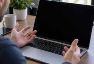 Laptop on a desk with a black screen and hands resting on the keyboard