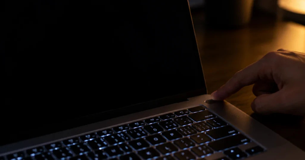 Finger holding the power button on a laptop with a black screen